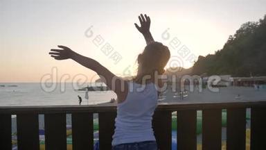 快乐的小女孩在海上张开双手享受自由。夕阳海边海滩，欢呼雀跃的女徒步旅行者张开双臂。